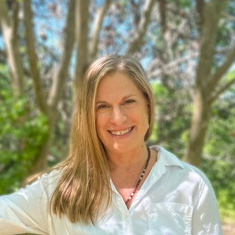 Banyan Water's CEO Gillan Taddune profile of smiling woman with blonde hair falling over one shoulder, white shirt, trees in the background.